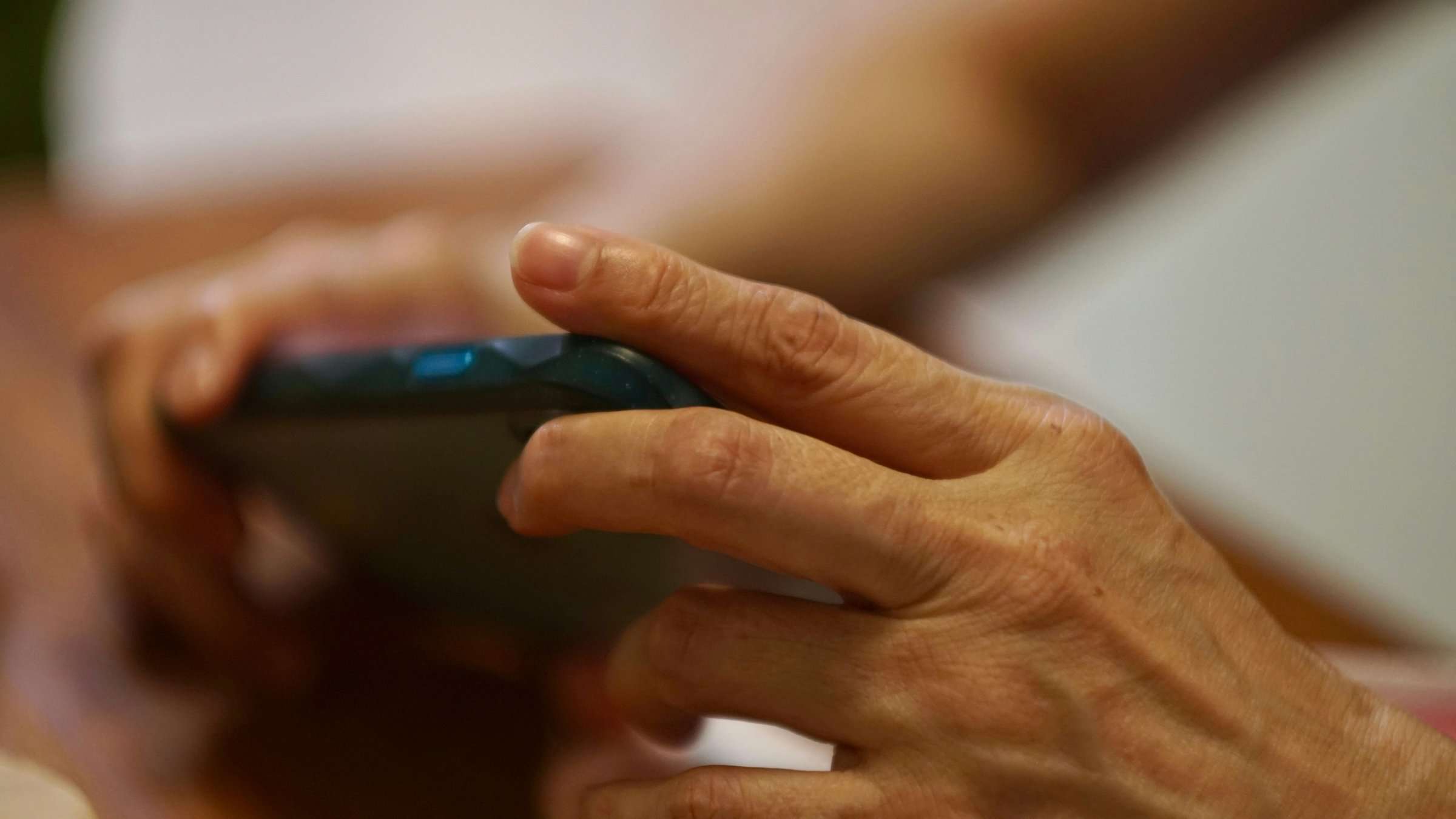 La mano de una persona mayor sostiene un teléfono móvil.