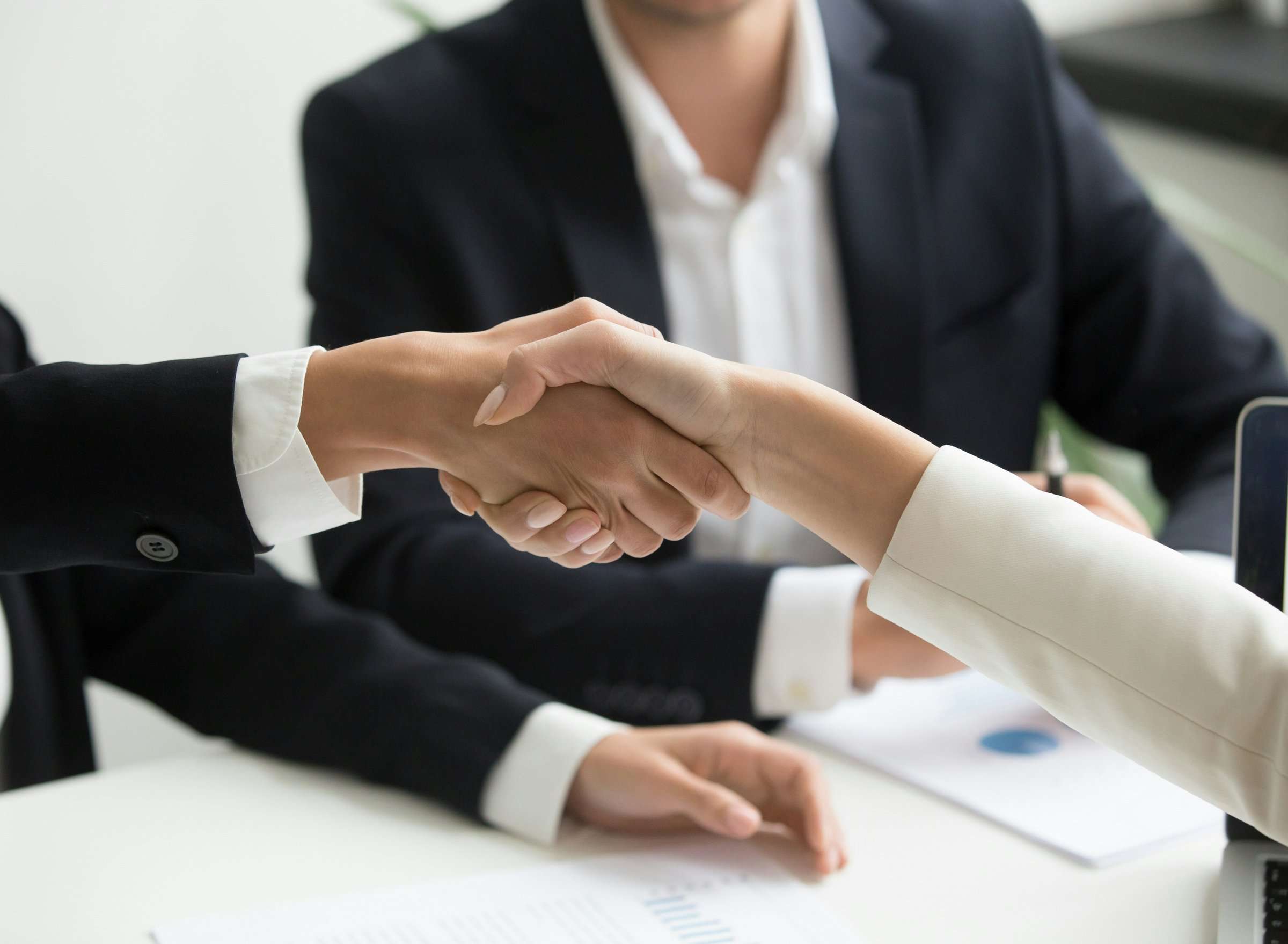 Dos profesionales se dan la mano sobre una mesa de trabajo.