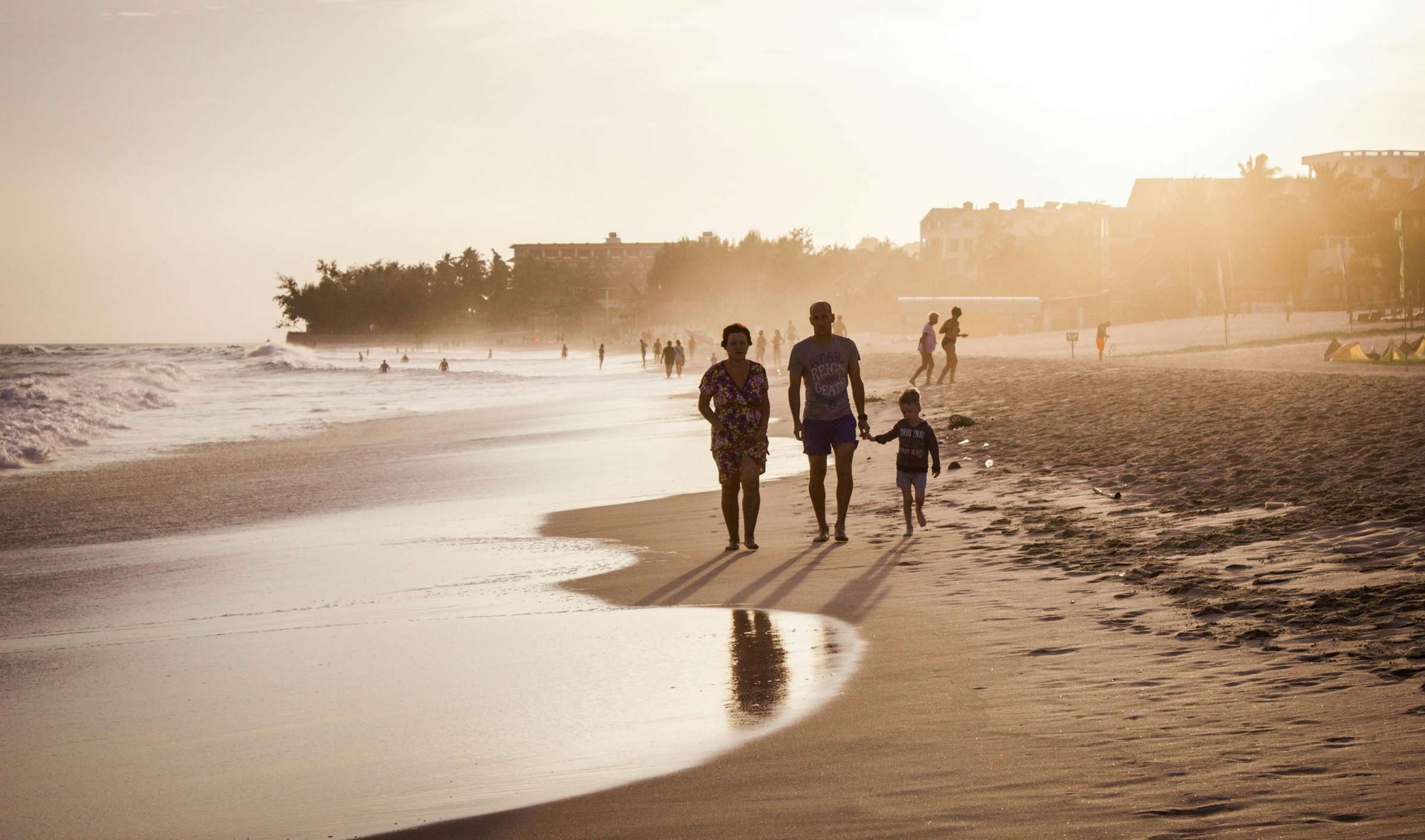 Una familia pasea de espaldas por la orilla del mar.